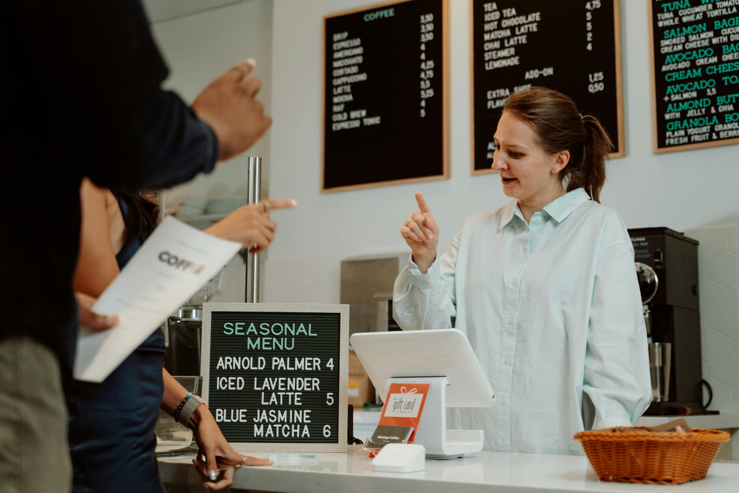Barista serving customers at cafe counter with seasonal menu board.