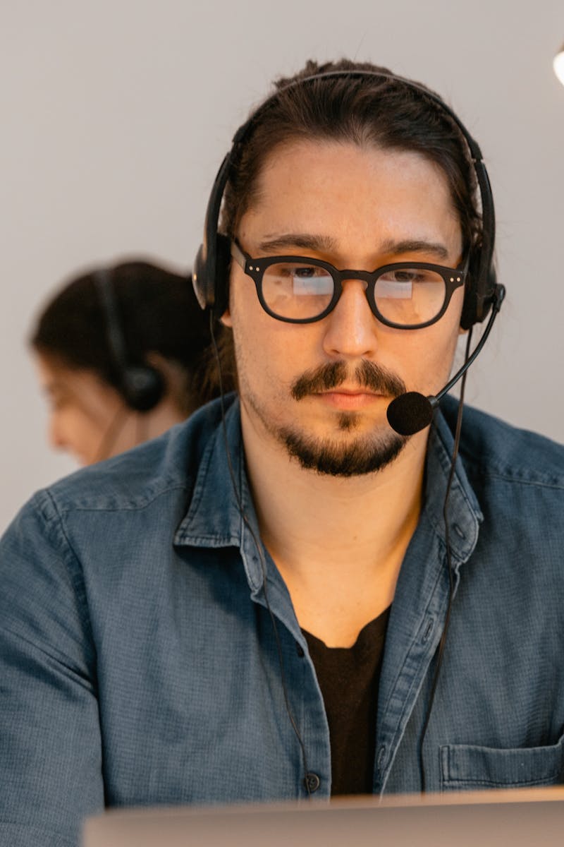 A call center agent wearing headphones, working intently at his desk in a modern office environment.